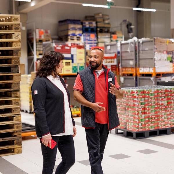 Im Filiallager: Kaufland-Verkaufsmitarbeiter im Gespräch mit einer Kollegin. Im Hintergrund ein Stapel Paletten.