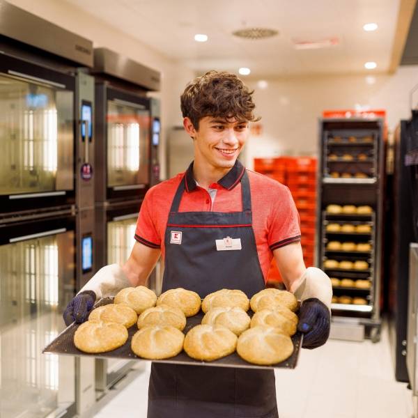 Junger Verkaufsmitarbeiter von Kaufland mit einem Blech frischgebackener Brötchen.