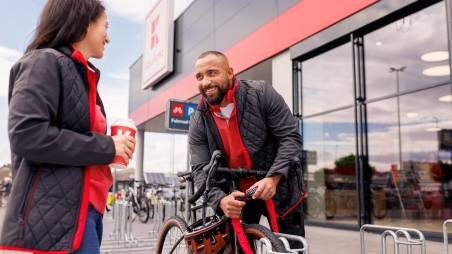 Pause vor der Kaufland-Filiale: Kaufland-Verkaufsmitarbeiter schließt sein Fahrrad an. Neben ihm eine Kollegin mit einem To-Go-Getränk bei der Pause.