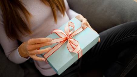 Frau sitzt auf einem Sofa und hält ein blau verpacktes Geschenk in der Hand.