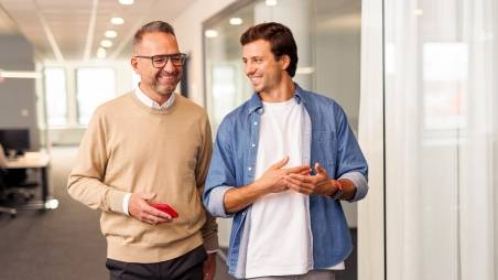 2 Kollegen auf dem Flur im Kaufland-Büro lachend im Gespräch.